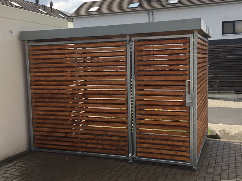 Ein Holzschuppen steht auf einem gemauerten Gehweg vor einem Haus