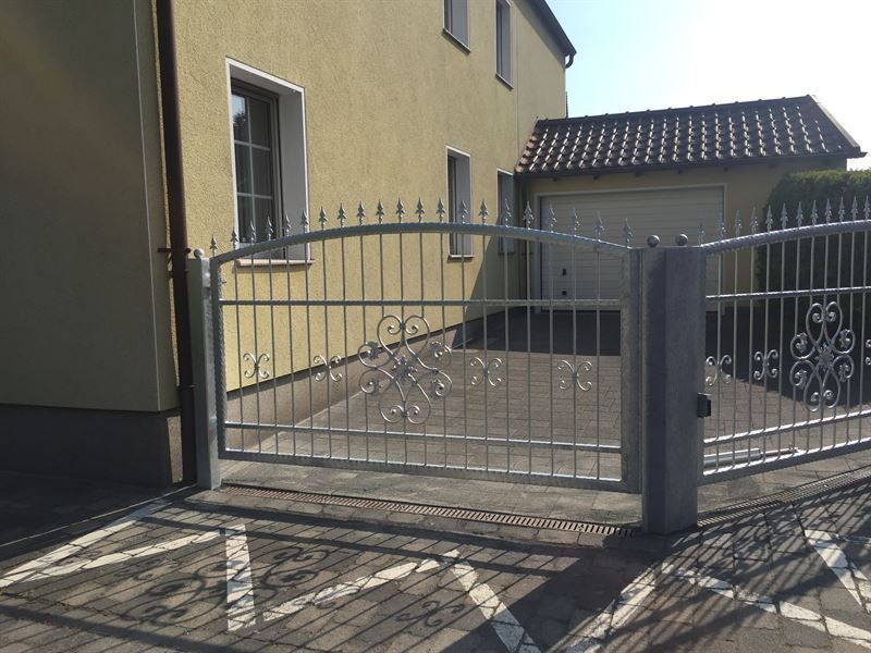 Ein schmiedeeisernes Tor steht vor einem gelben Haus