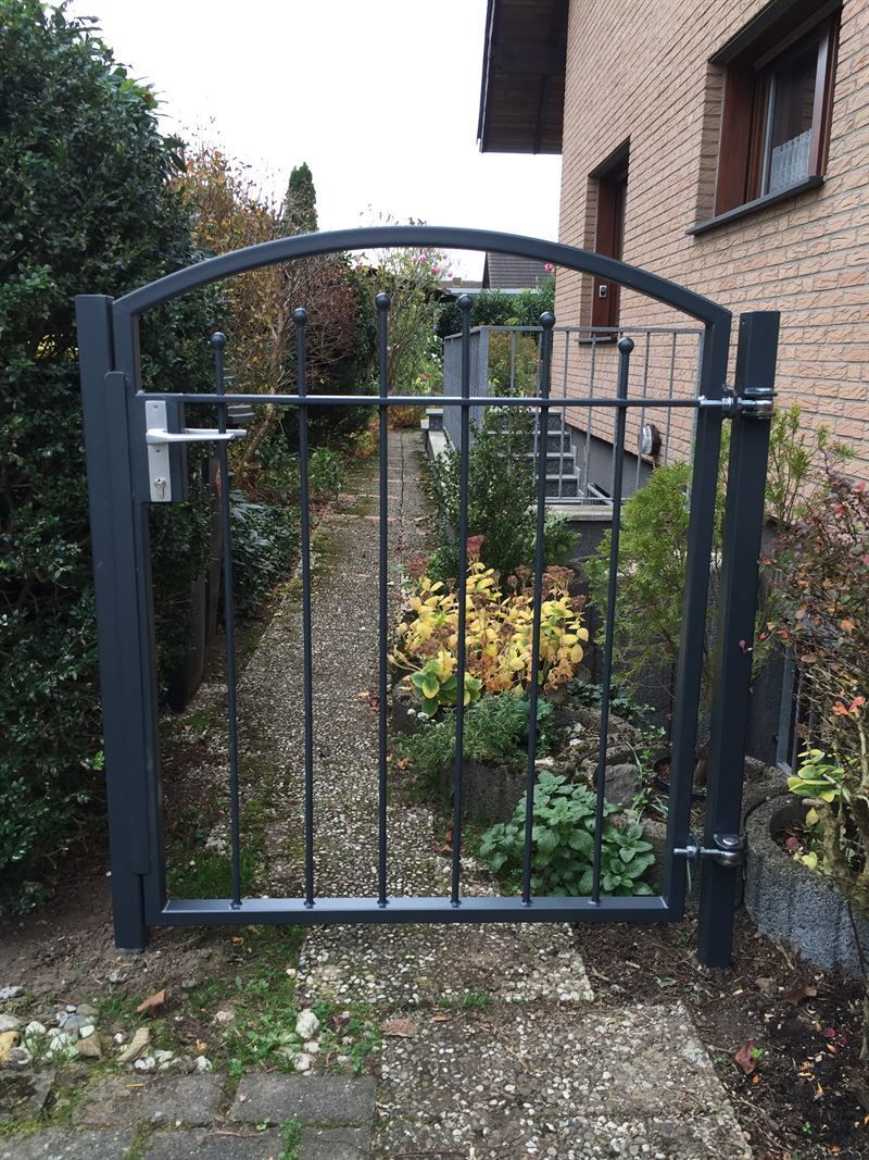 Vor einem Backsteinhaus steht ein schwarzes Tor.