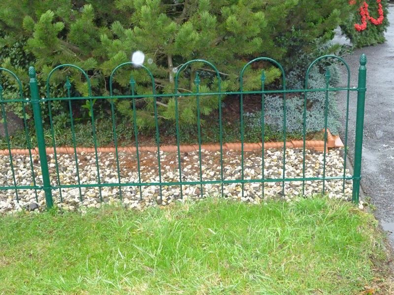 Ein grüner Metallzaun umgibt eine Kiesbereich in einem Hof.