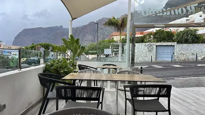 Terraza de café al aire libre con mesas y sillas bajo sombrillas, con vistas a las montañas en un día lluvioso.