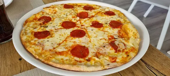 Pizza de pepperoni en un plato blanco sobre una mesa de madera.
