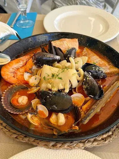 Guiso de mariscos con mejillones, camarones, almejas y pasta en un tazón negro sobre una mesa.