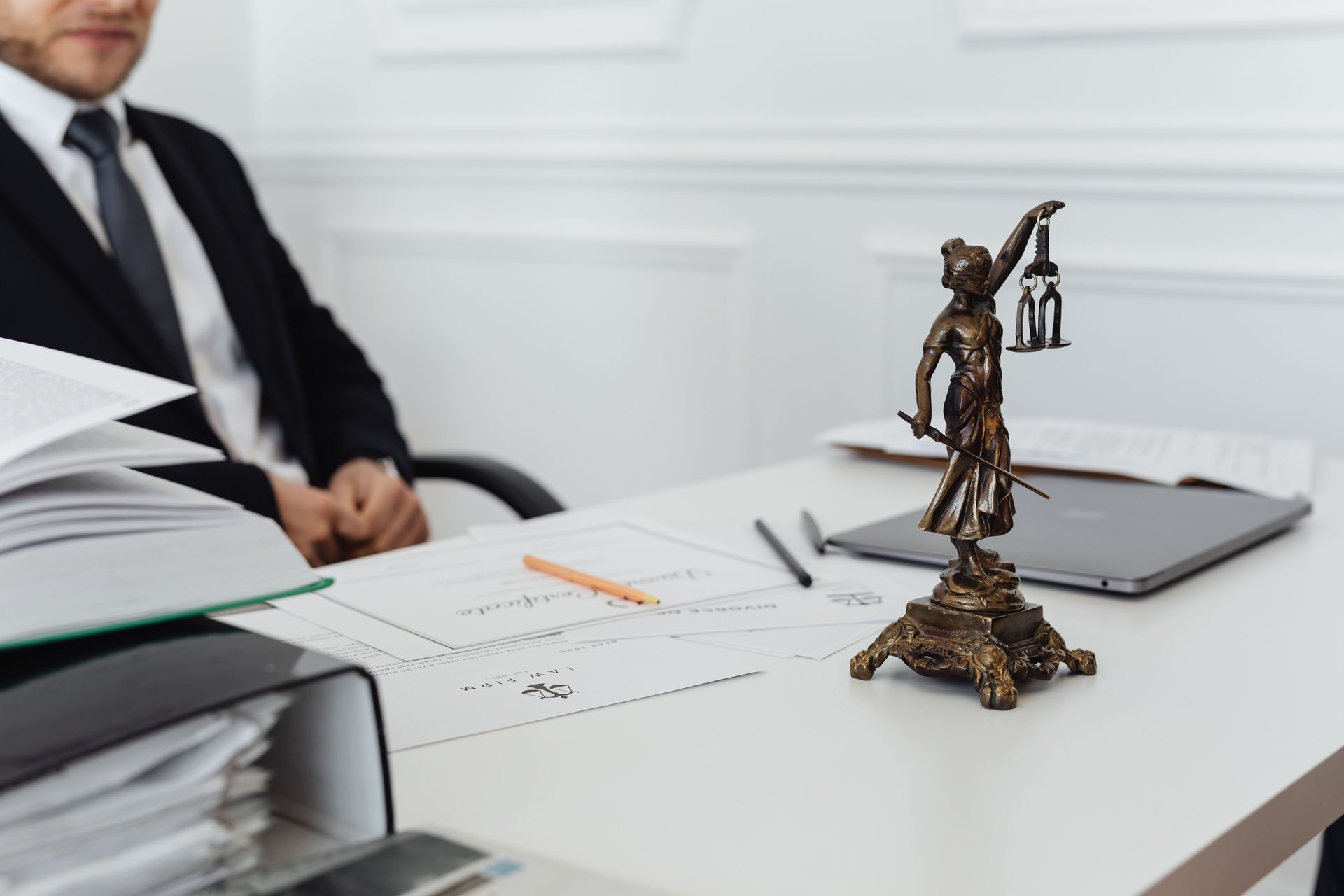 Escritorio con documentos legales, ordenador portátil y una figura de la Dama de la Justicia en primer plano.