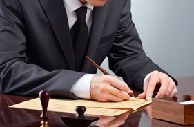 Un hombre con traje y corbata está escribiendo en un trozo de papel.