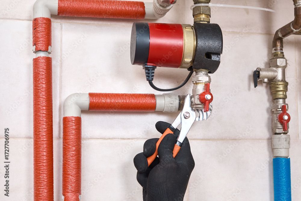 Eine Person, die mit einer Zange an Wasserrohren arbeitet.