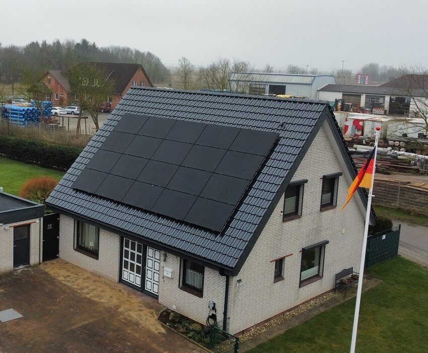 Ein braunes Ziegeldach geht in ein flaches, dunkelgraues Dach über, im Hintergrund sind Gebäude zu sehen.