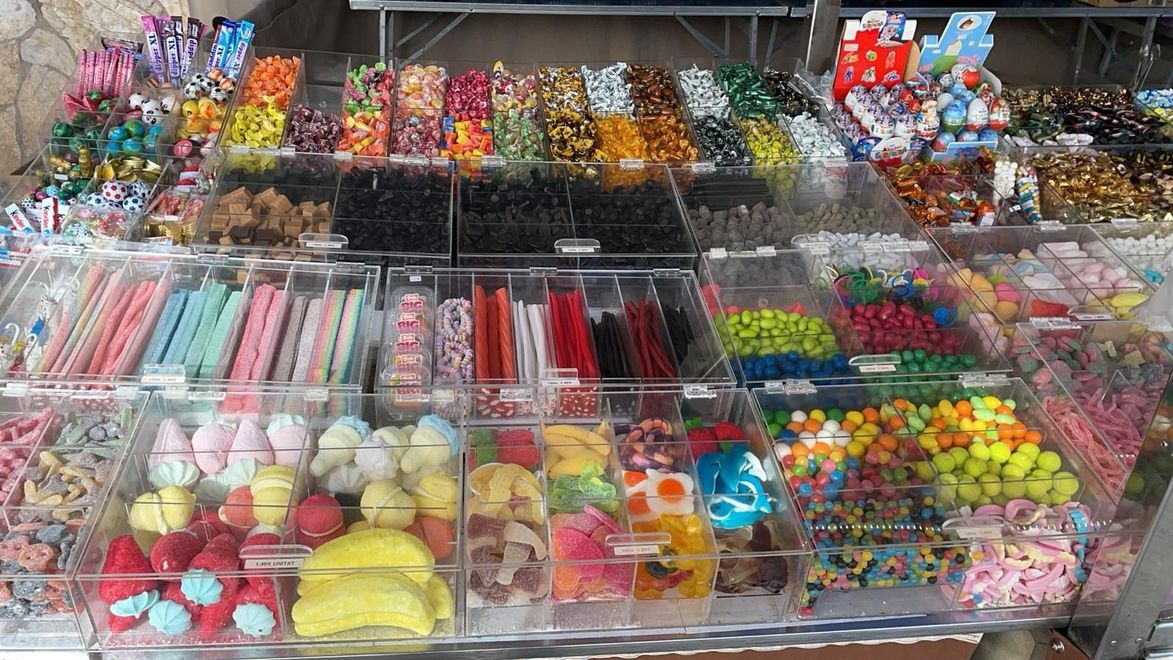 Una exhibición de varios dulces coloridos en contenedores transparentes en una tienda, incluidos gomitas, chocolates y regaliz.