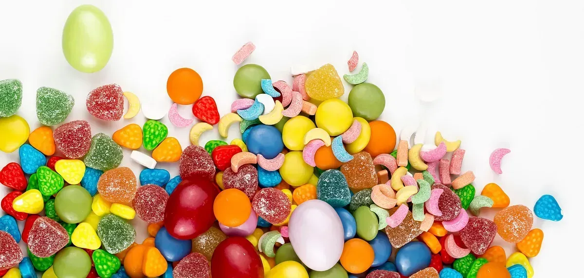 Una pila de dulces coloridos, incluyendo gomitas, pastillas de goma y huevos de chocolate recubiertos, sobre un fondo blanco.