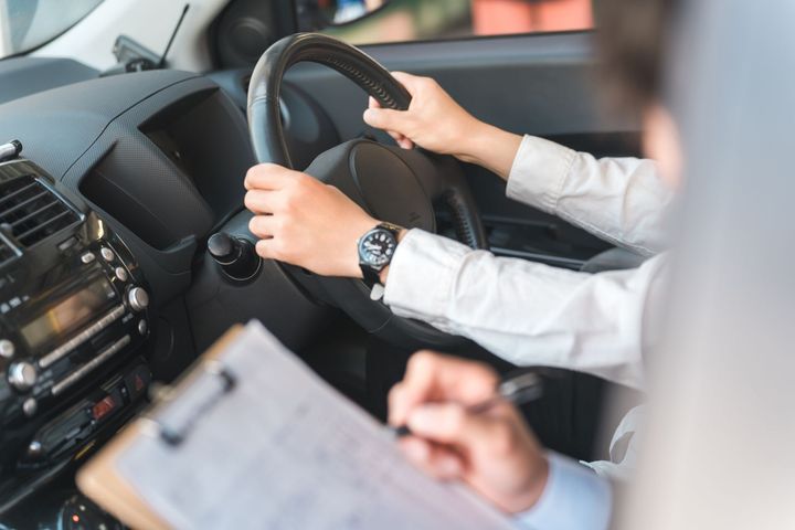 Le conducteur tient le volant d'une voiture tandis qu'une autre personne prend des notes à côté de lui.