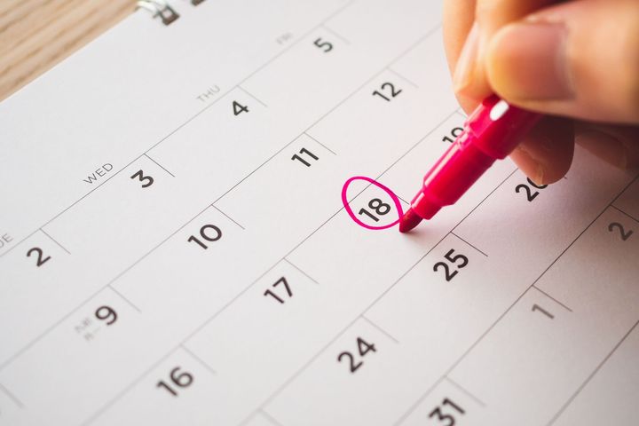 Main entourant le 18 sur un calendrier avec un marqueur rouge.