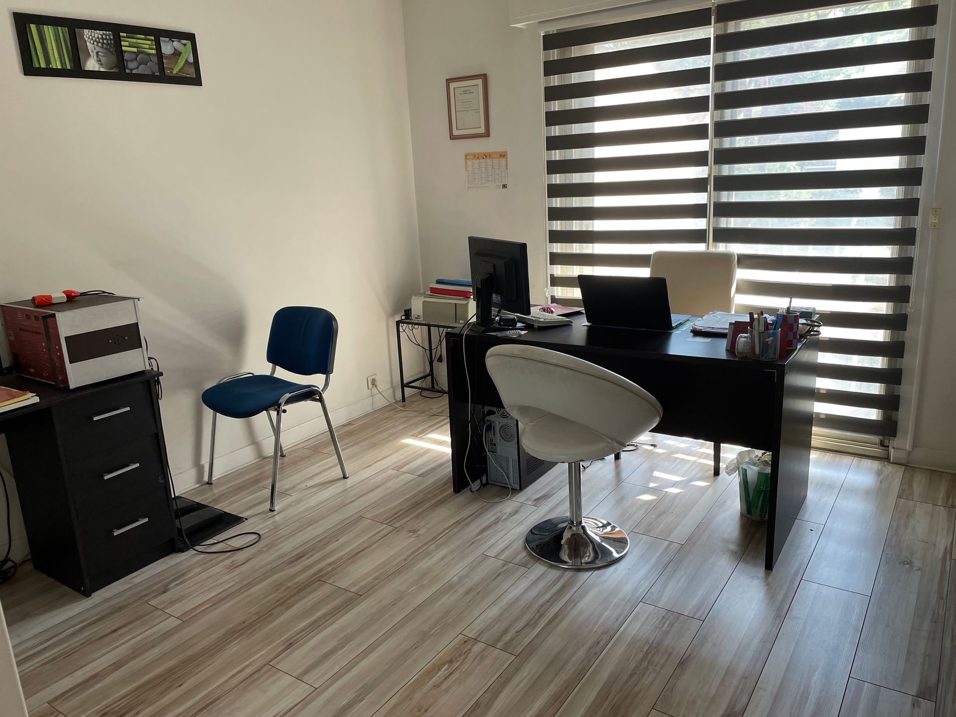 Petit bureau à domicile avec un bureau, une chaise, un classeur et des stores rayés.