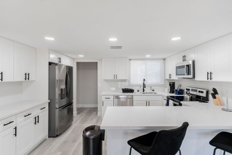 Bright white modern kitchen with stainless steel appliances, island, and open workspace