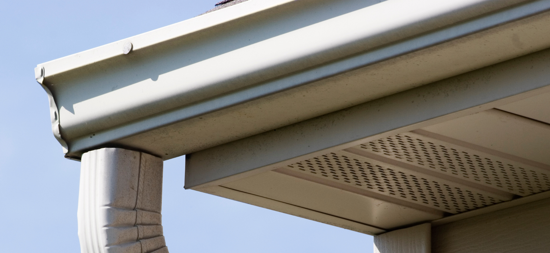Gros plan sur une gouttière et un soffite de maison, avec une descente pluviale sur fond de ciel dégagé.