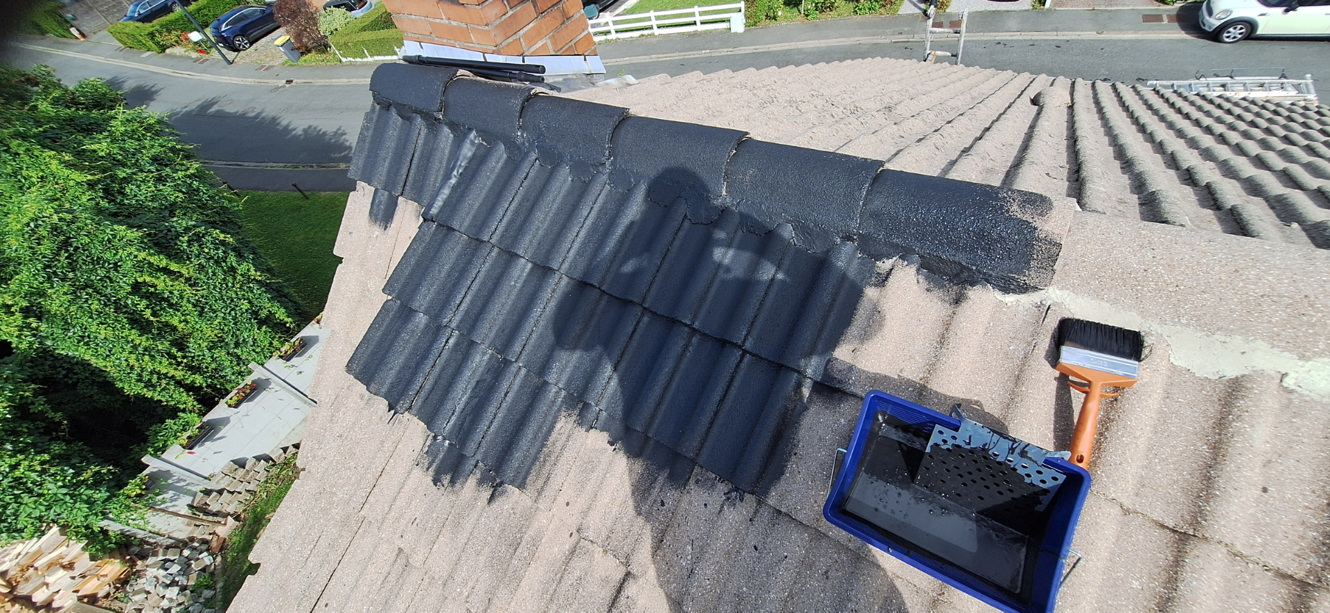 Un toit recouvert de tuiles peintes en noir ; un bac à peinture et un pinceau sont posés sur le toit.