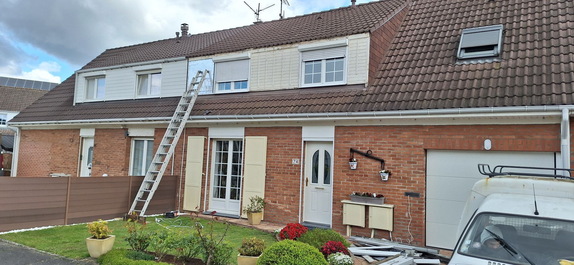 Façade de maison en rénovation, échelle appuyée contre le toit, façade en briques rouges et ciel nuageux.