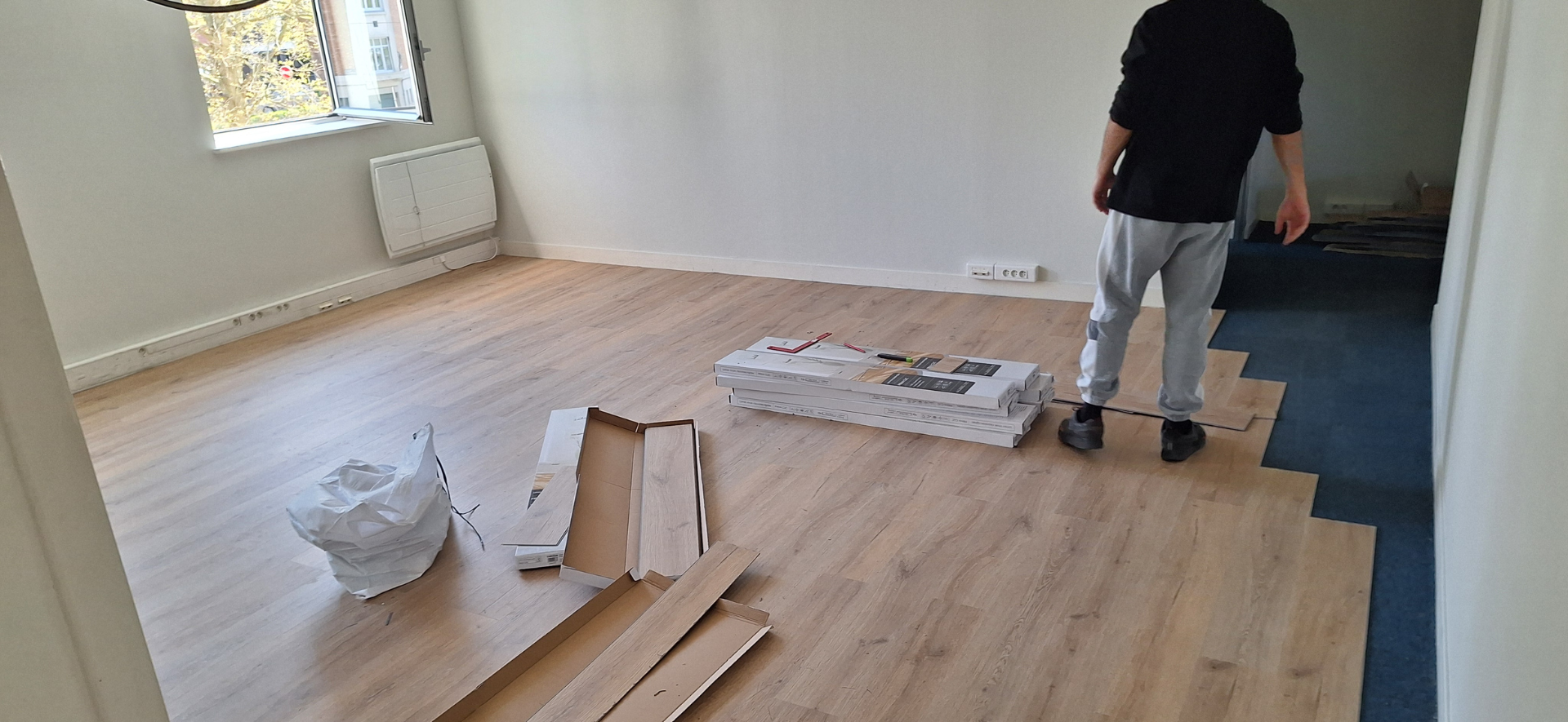 Une personne pose du parquet dans une pièce avec fenêtre. Le parquet est en bois clair.