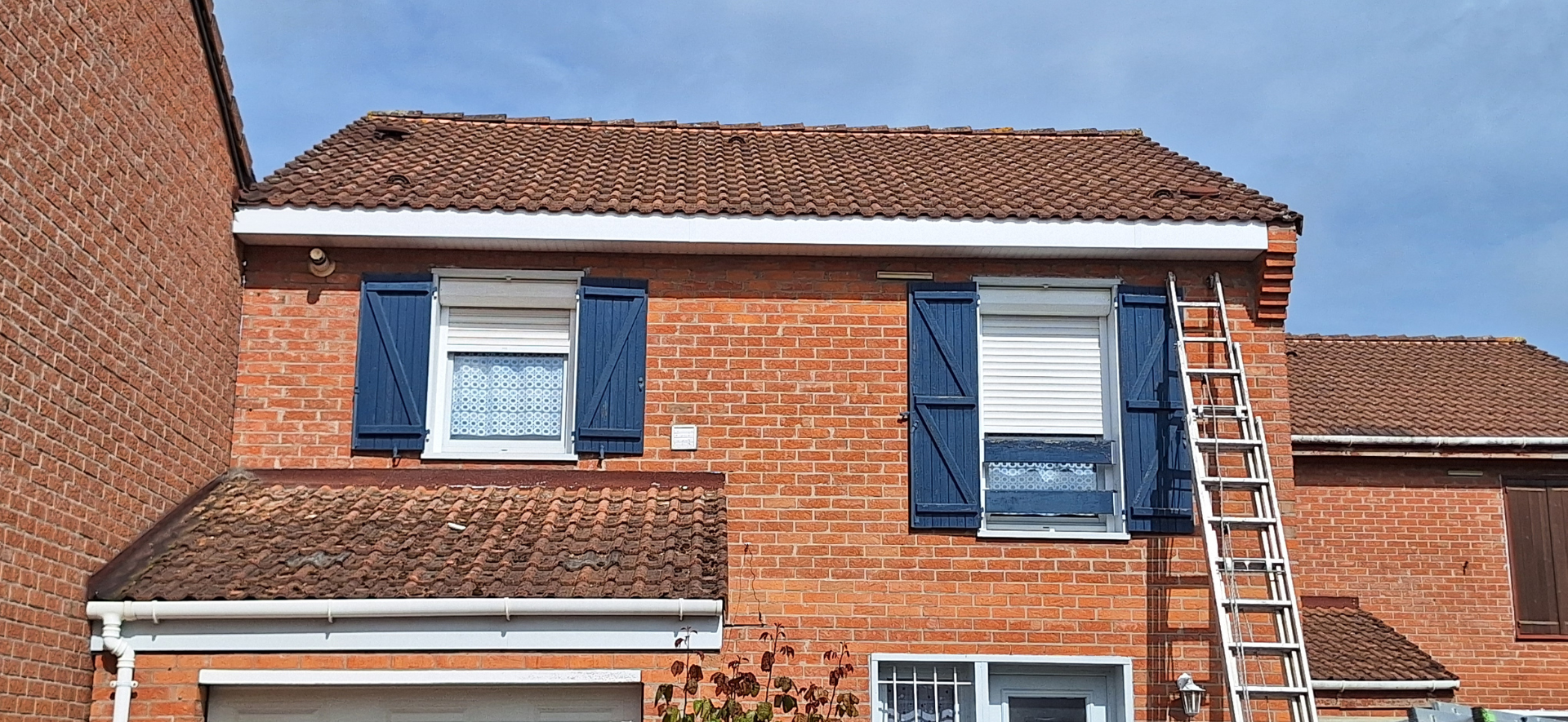Bâtiment en briques avec des volets bleus et une échelle appuyée contre le toit.