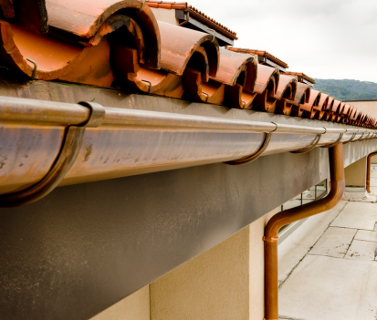 Toiture brune avec tuiles en terre cuite, gouttières et descente pluviale en cuivre.