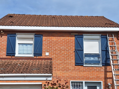 Maison en briques rouges avec des volets bleus, une échelle.