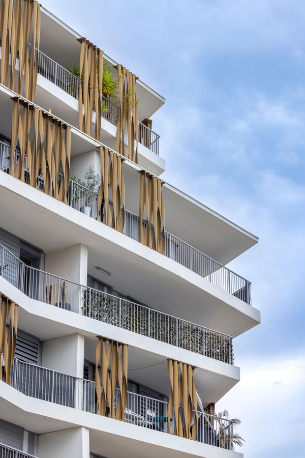 Bâtiment blanc à plusieurs étages avec balcons, accents en bois et ciel bleu.