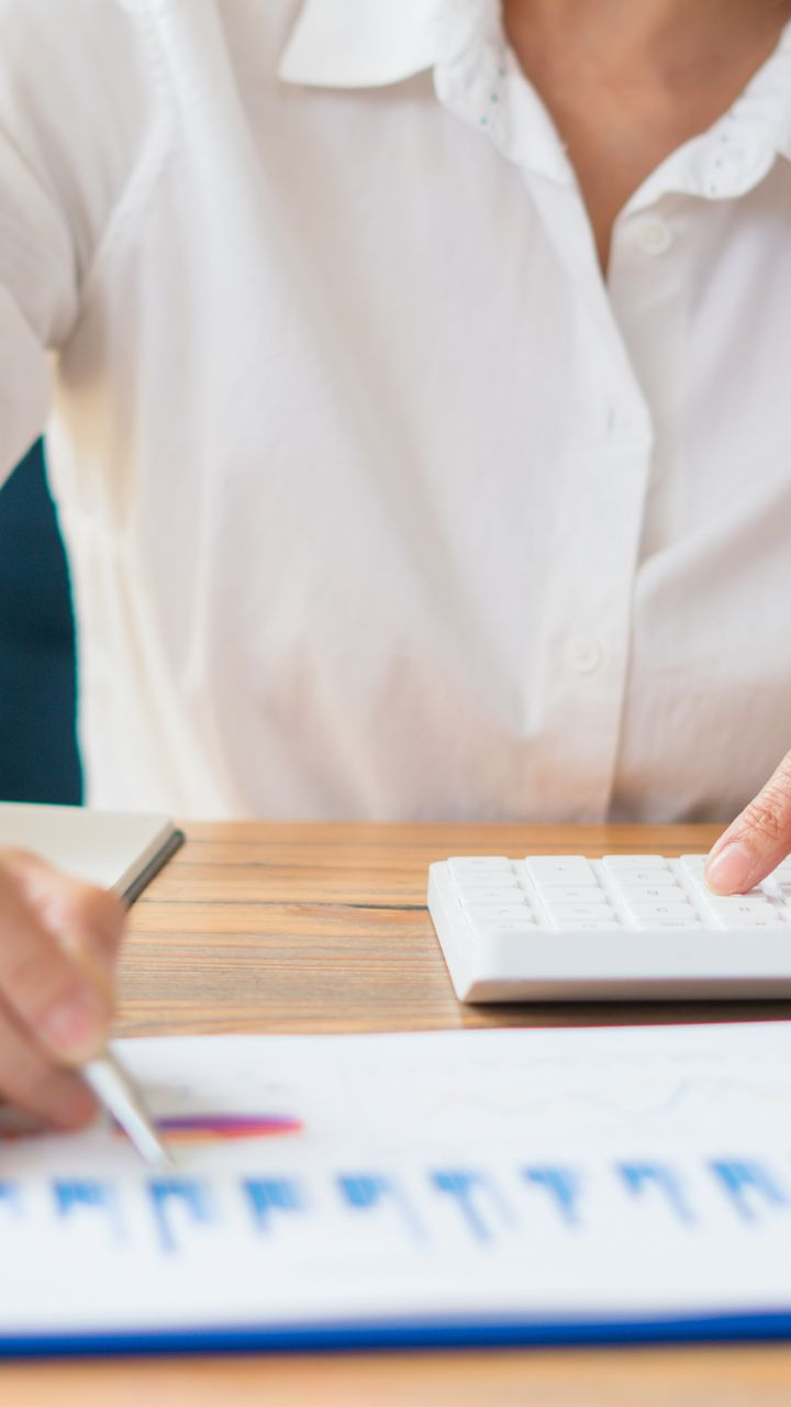 Personne en chemise blanche utilisant une calculatrice et un stylo, analysant un graphique bleu et rouge sur un bureau en bois.