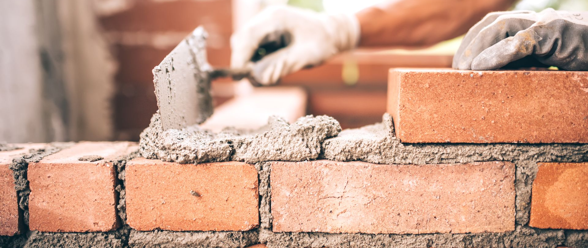 Maçon utilisant une truelle pour appliquer du mortier entre des briques rouges, construisant un mur.
