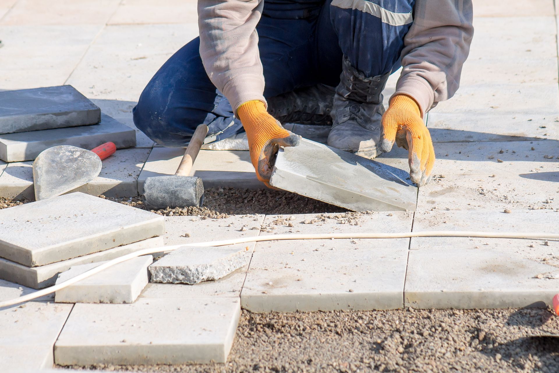 Une personne portant des gants pose des pavés sur une surface en béton à l'extérieur.
