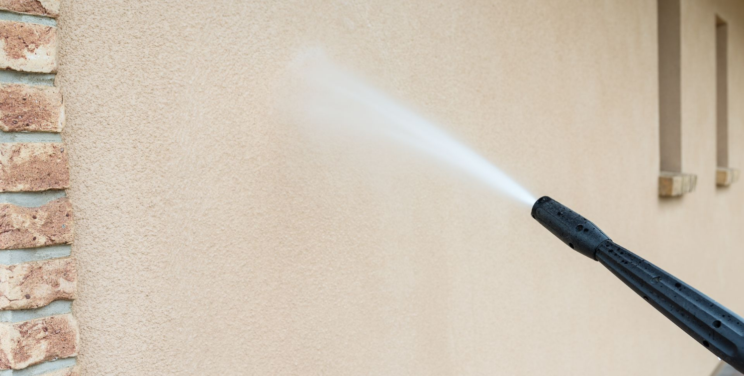 Nettoyage au nettoyeur haute pression d'un mur en stuc brun clair.