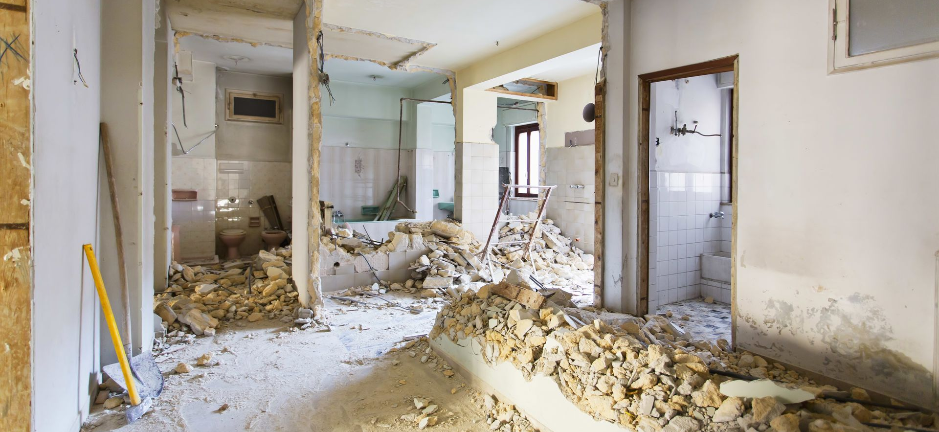 Démolition intérieure, gravats éparpillés sur le sol, murs partiellement enlevés, porte visible.