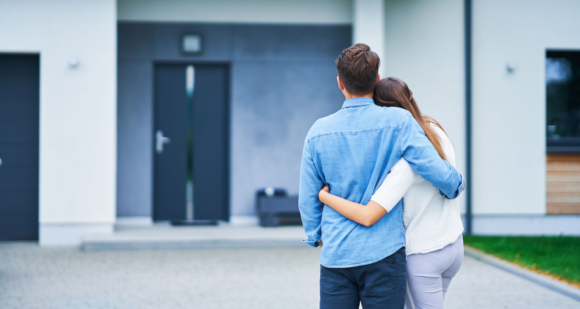 Couple enlacé regardant vers leur nouvelle maison avec un extérieur bleu et blanc.