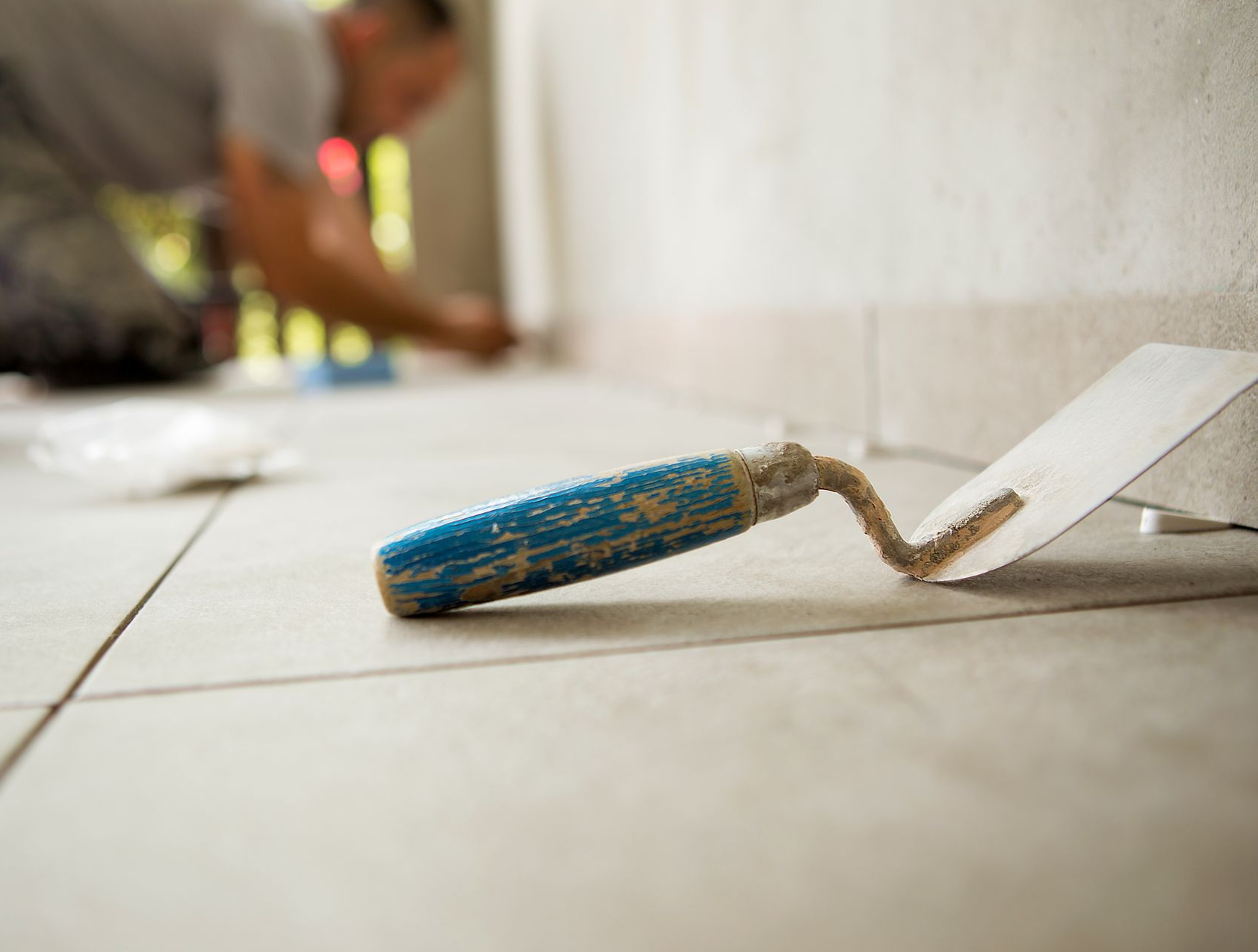 Truelle sur un sol carrelé avec une personne posant des carreaux en arrière-plan.