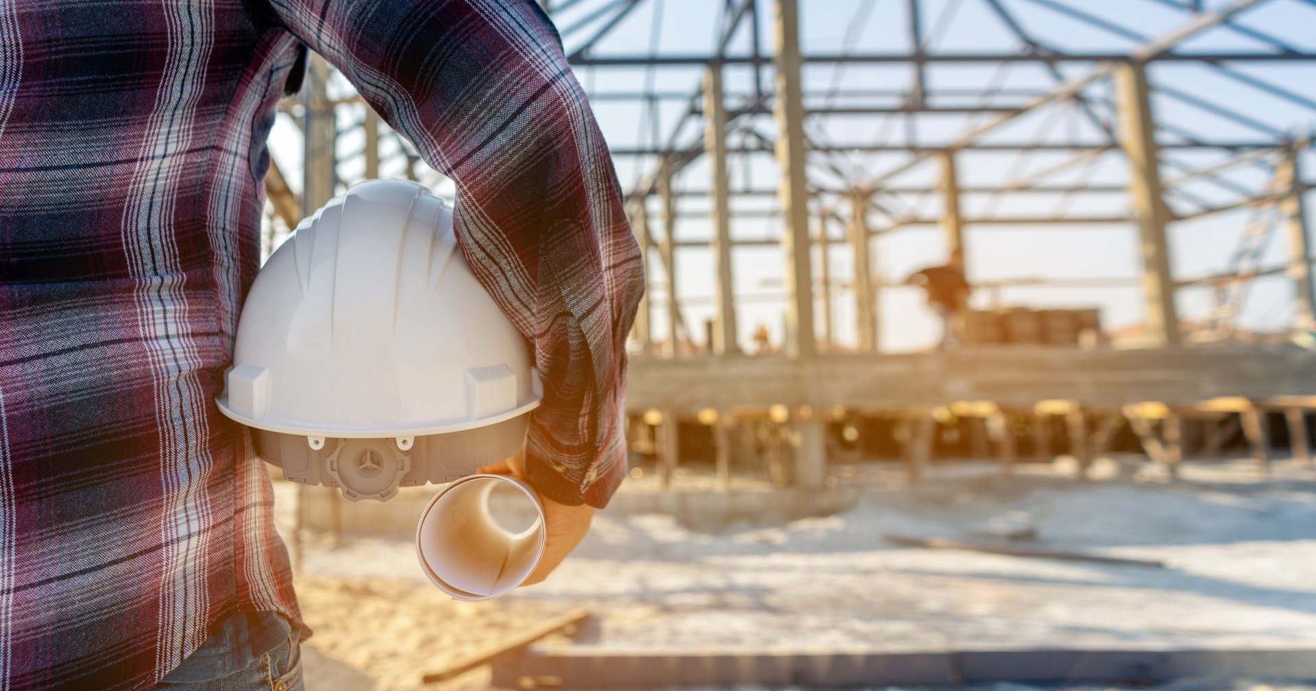 Ouvrier du bâtiment sur un chantier, tenant un casque blanc et des plans d'architecture.
