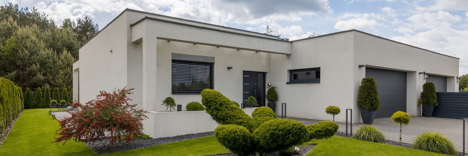Maison blanche moderne avec pelouse bien entretenue, arbustes et portes de garage.