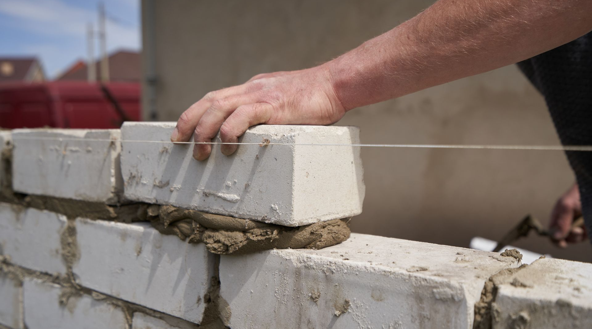 Personne posant des briques blanches avec du mortier, à l'aide d'un guide-fil et d'un marteau.