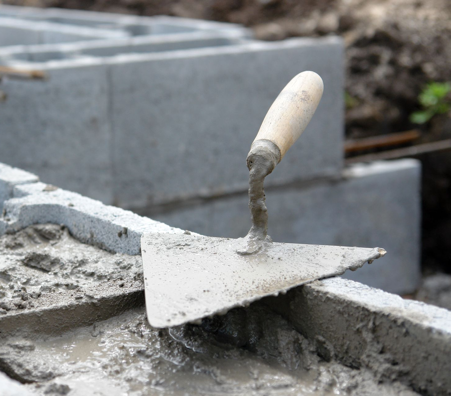 Truelle posée sur du mortier ; blocs de béton en arrière-plan ; chantier de construction.