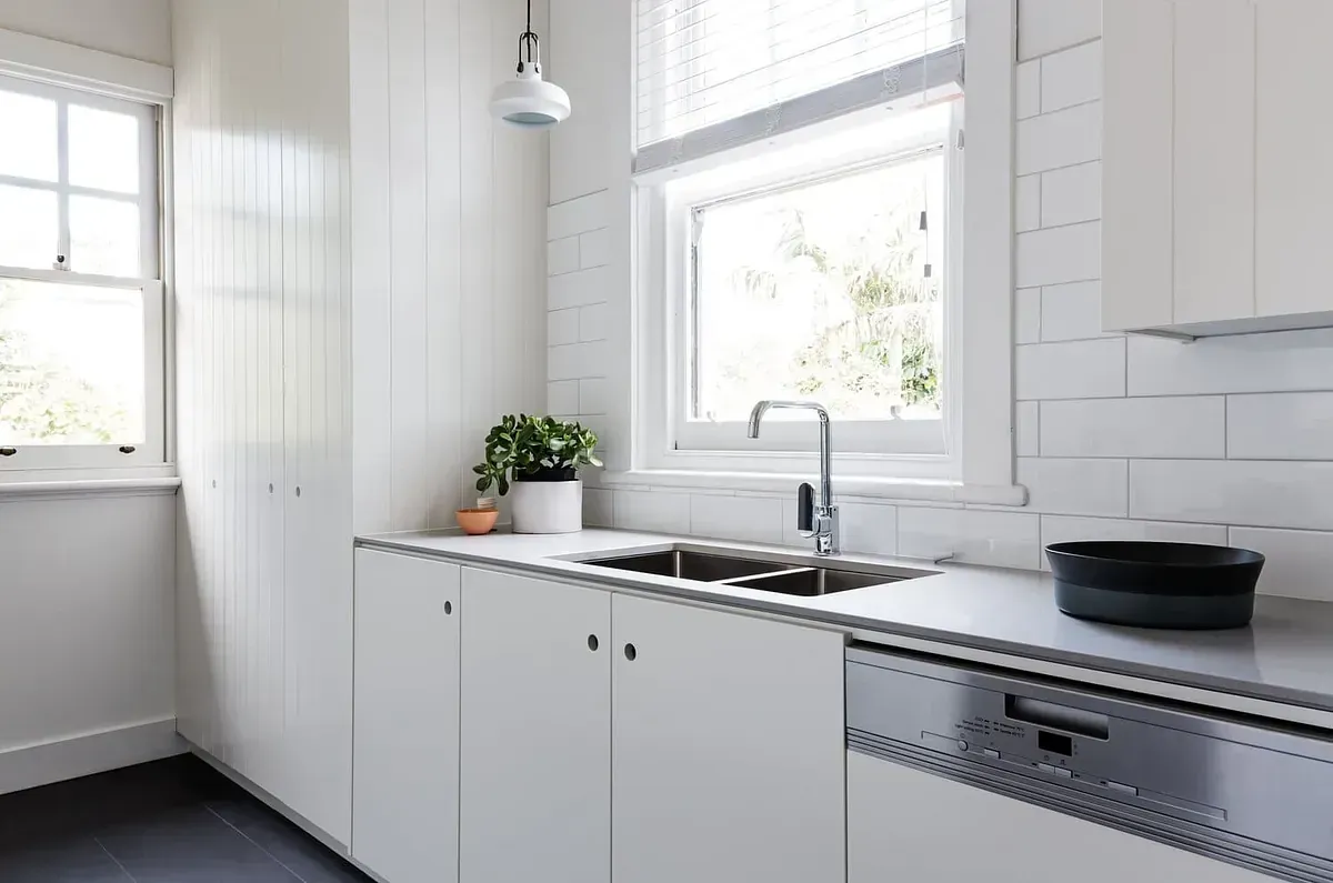 Una cocina con gabinetes blancos, un fregadero y una ventana.
