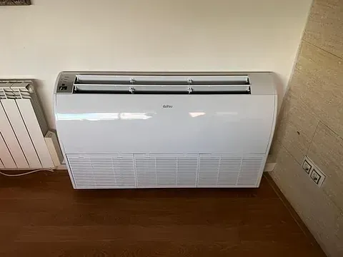 Un acondicionador de aire blanco está sobre un piso de madera en una habitación al lado de un radiador.
