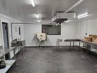 Una gran habitación vacía con mesas de acero inoxidable y un fregadero.