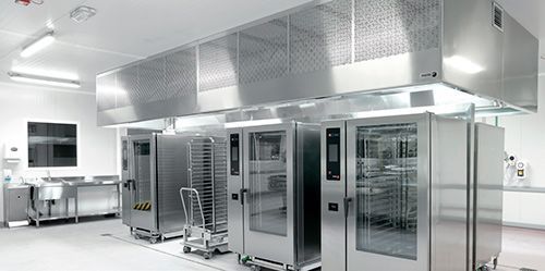 Una fila de hornos de acero inoxidable están alineados en una cocina.