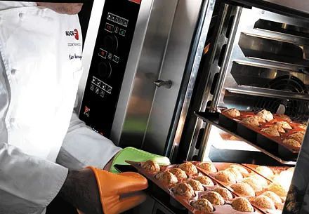 Un chef está sacando una bandeja de muffins de un horno.