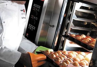 Un chef está sacando una bandeja de muffins de un horno.