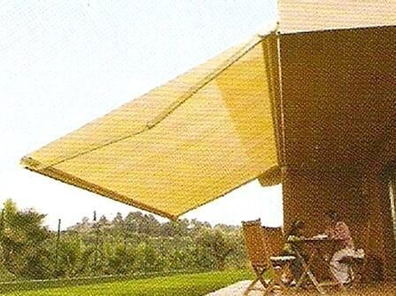 Toldo amarelo estendendo-se sobre um pátio ao lado de um prédio, com cadeiras e mesa ao ar livre com vista para a vegetação.