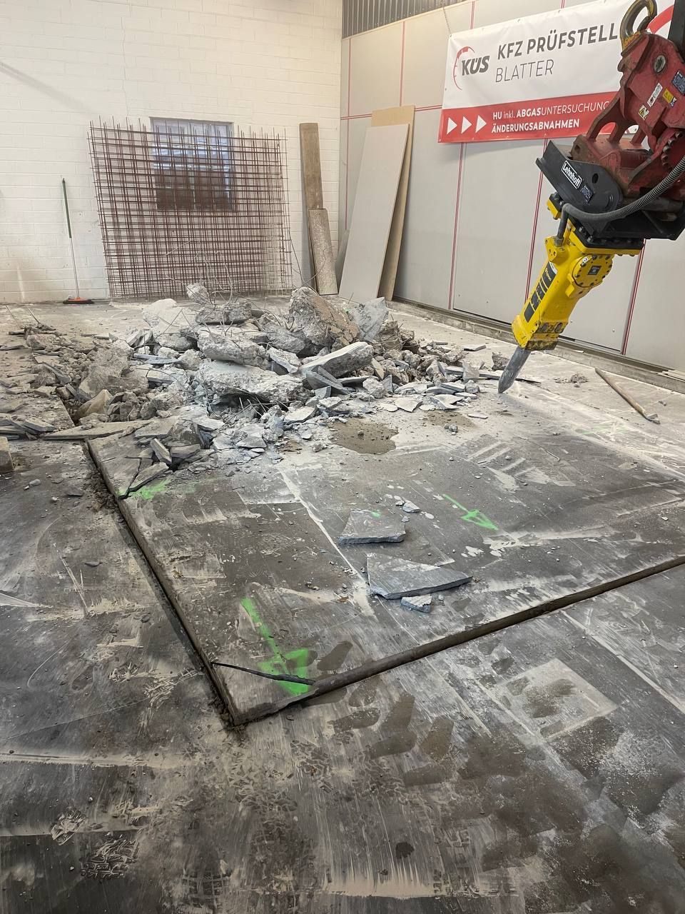 Baustelle mit Schutt auf dem Boden und einem gelben Baggerarm, der im Inneren eine Wand abreißt.