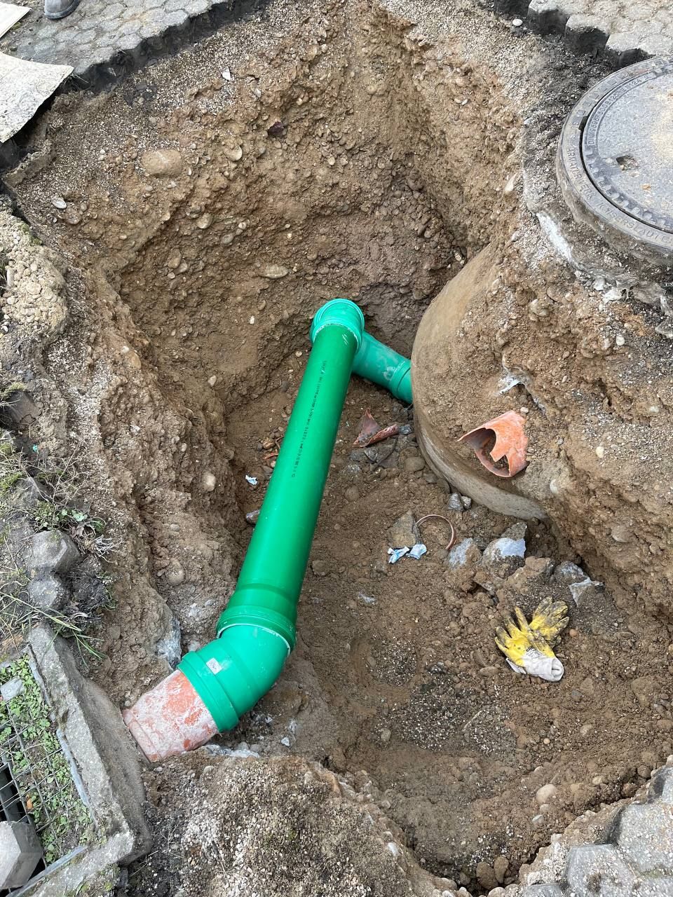 Grünes Rohr, verlegt in einer Erdbaugrube neben einer Betonöffnung für Versorgungsleitungen.