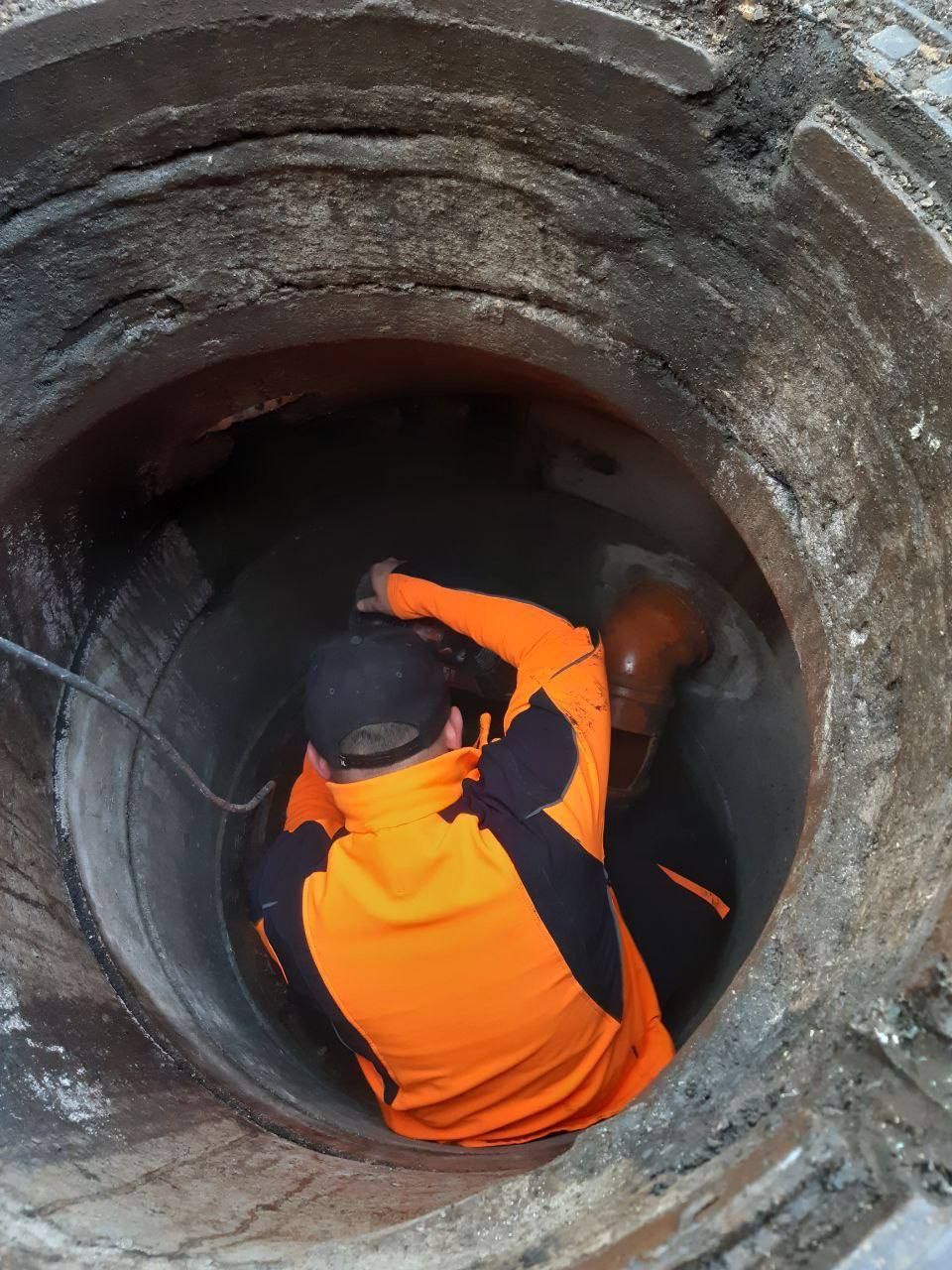 Ein Arbeiter in orangefarbener Schutzkleidung betritt ein großes Betonrohr oder einen Tunnel.