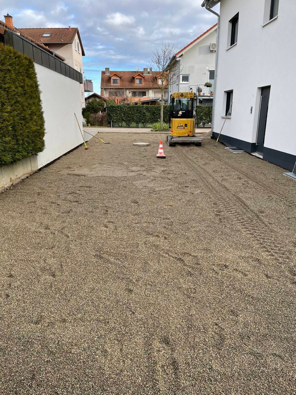 Kieshof zwischen weißen Gebäuden, in dessen Mitte eine gelbe Baumaschine steht.