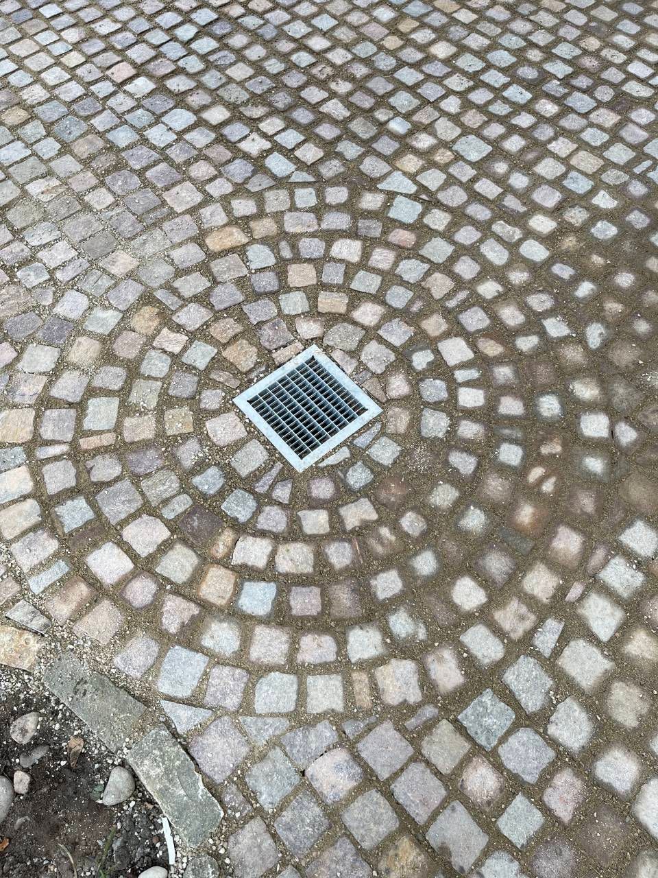 Kopfsteinpflaster mit einem kleinen quadratischen Metallablaufgitter in der Mitte
