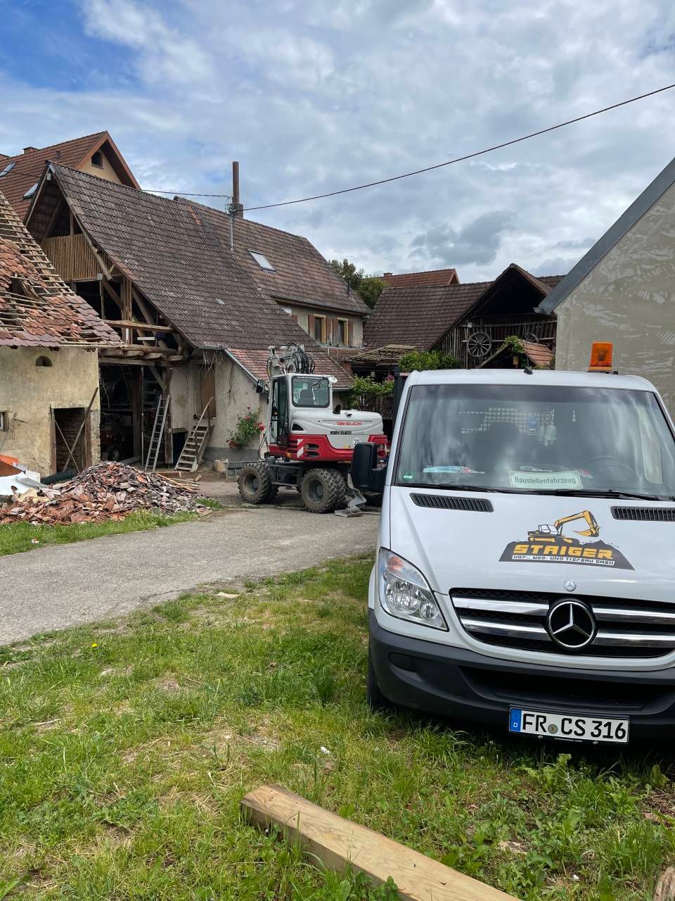 Beschädigtes Haus und Trümmer mit einem roten Traktor und einem weißen Mercedes-Transporter in einem ländlichen Hof