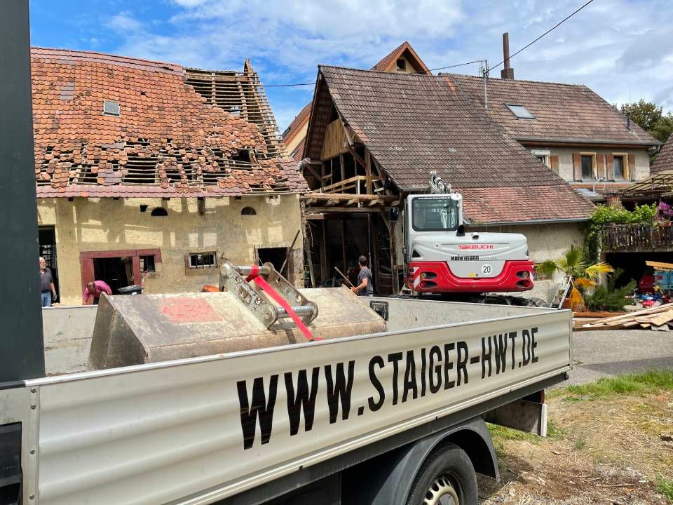 Abrissgelände mit einem LKW-Anhänger, Schutt und beschädigten Häusern mit eingestürzten Dächern.